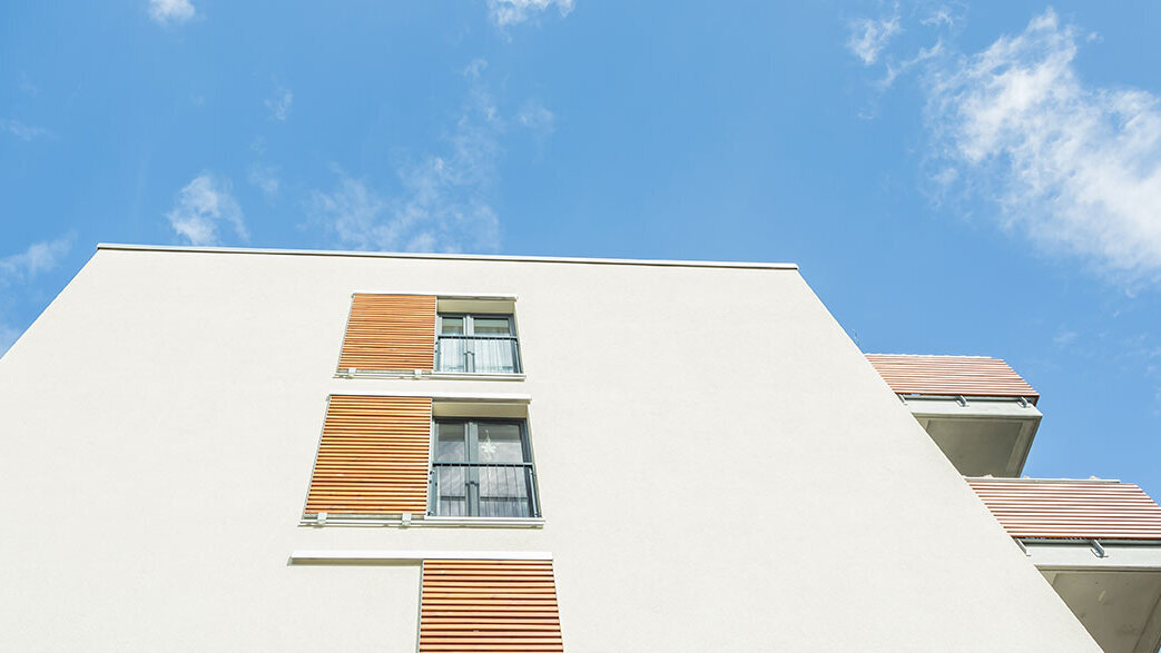 Helle Wohnhausfassade in Jena mit farbigen Fensterelementen und blauem Himmel